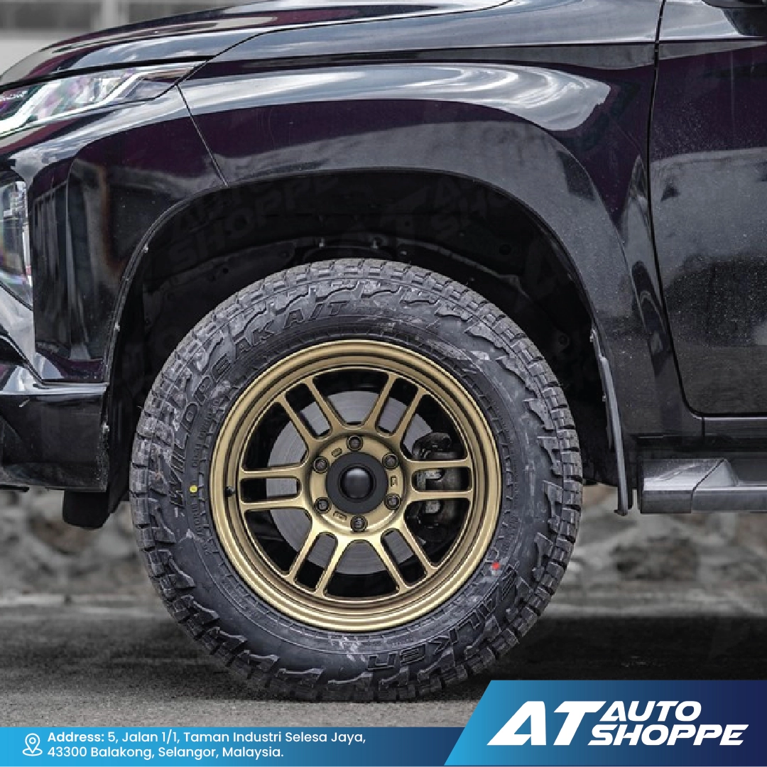 Close-up of a black vehicle with a gold rim on a road, featuring AT Auto Shoppe branding.