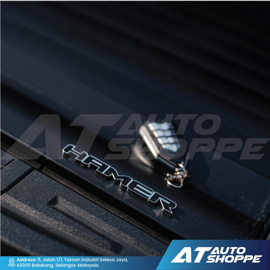Close-up of a car door handle with 'Hamer' branding on a black surface, featuring AT Auto Shoppe logo.