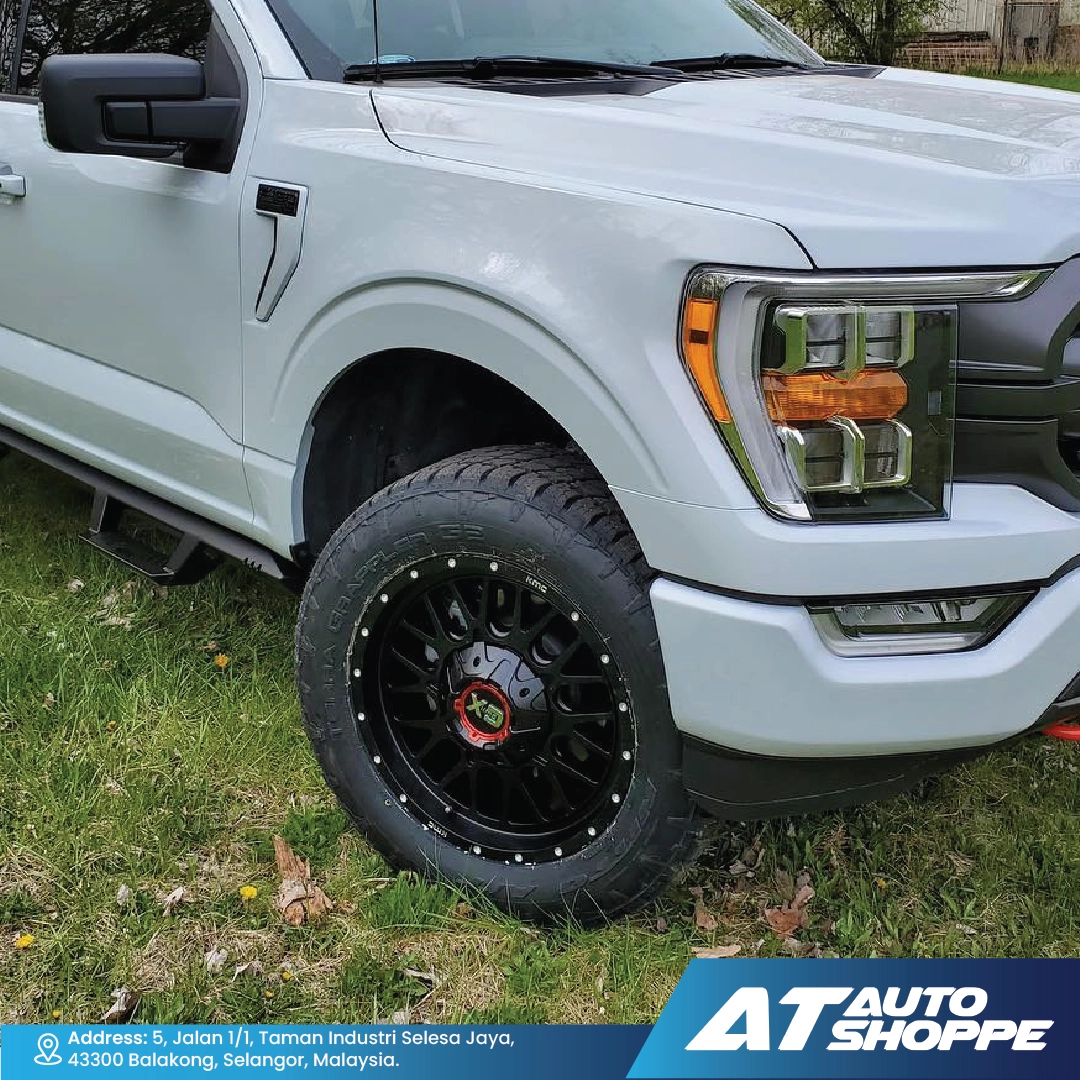 White pickup truck with black XD wheels on grass, featuring AT Auto Shoppe branding.