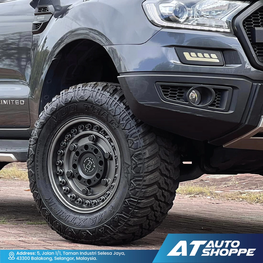 Close-up of a truck tire with off-road tread pattern on a rugged terrain, featuring AT Auto Shoppe branding.
