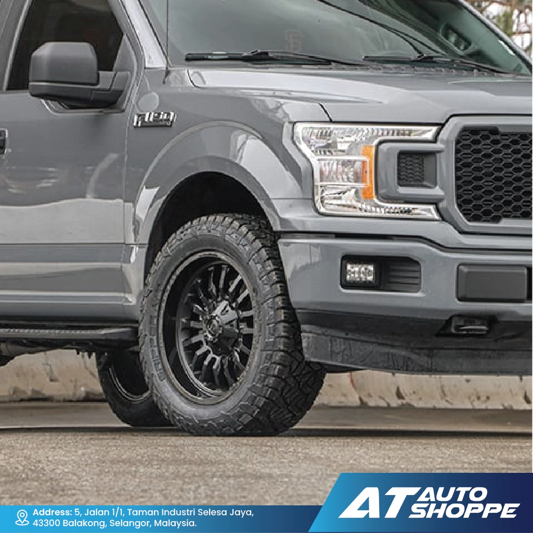 Gray pickup truck with off-road tires on a road, featuring AT Auto Shoppe branding.