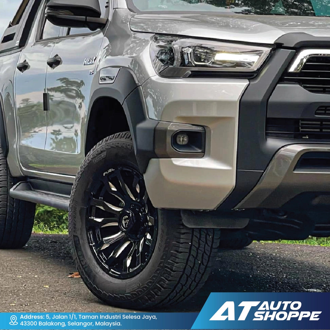 Close-up of a silver pickup truck with black wheels on a road, featuring AT Auto Shoppe branding.
