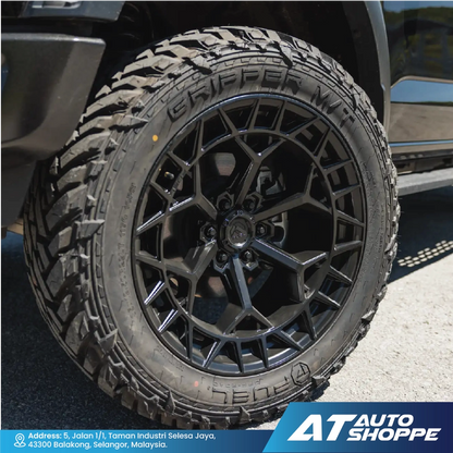 Close-up of a black tire with tread pattern on a vehicle, featuring the AT Auto Shoppe logo.