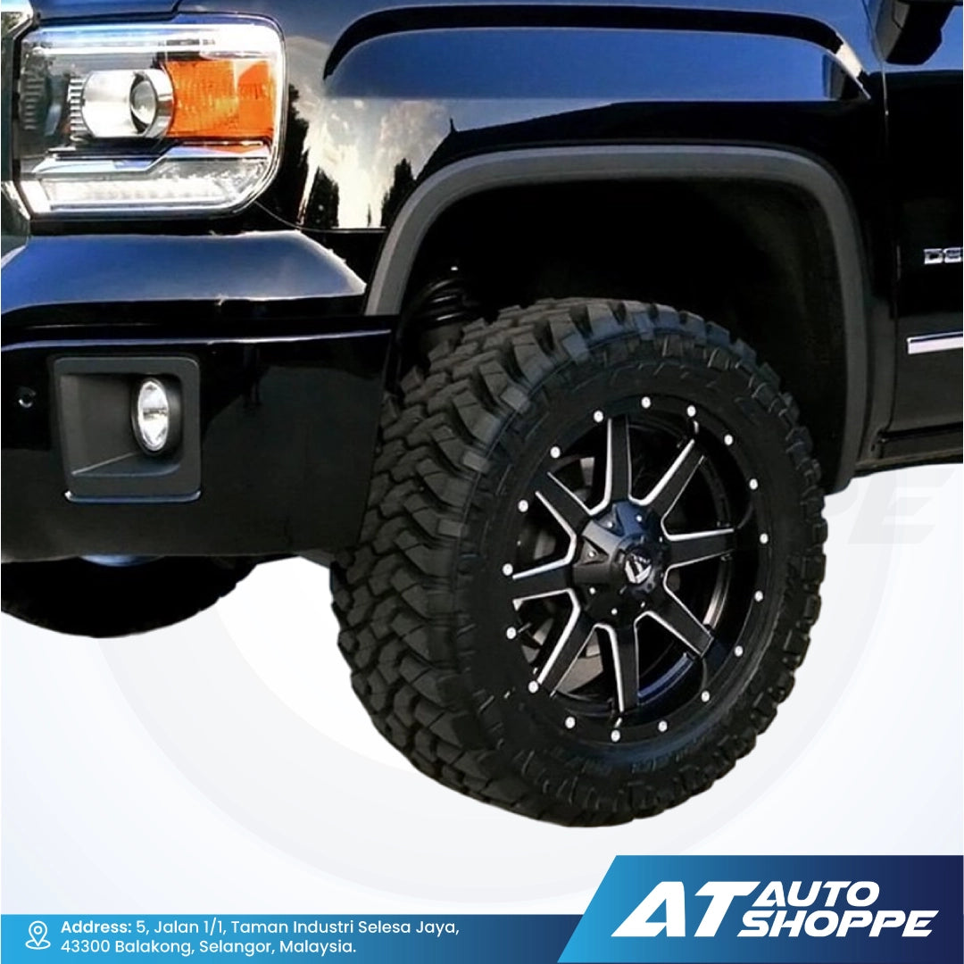 Close-up of a black truck tire with off-road tread pattern on a white background, featuring AT Auto Shoppe branding.