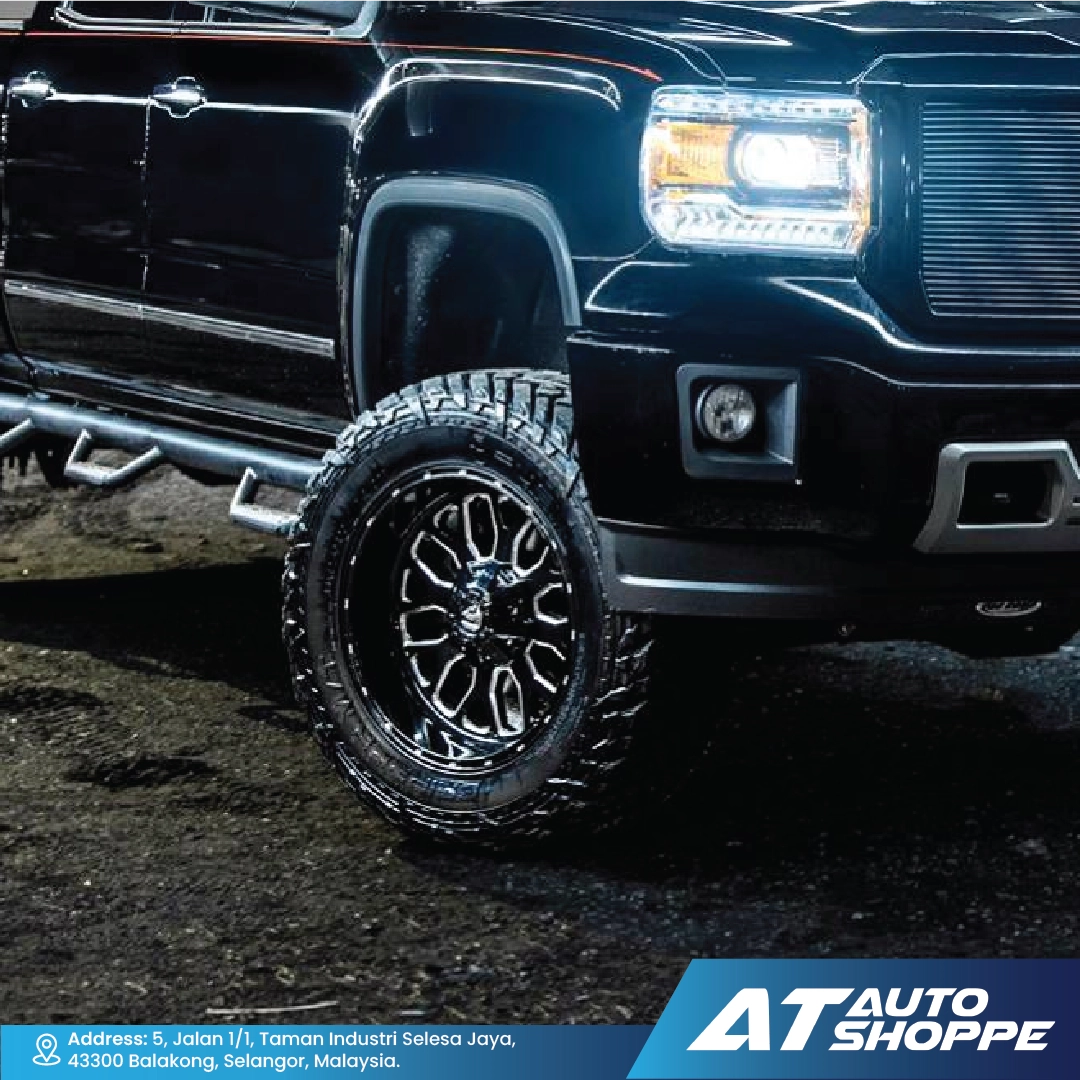 Close-up of a black truck with large off-road tires on a dark surface, featuring the AT Auto Shoppe logo.