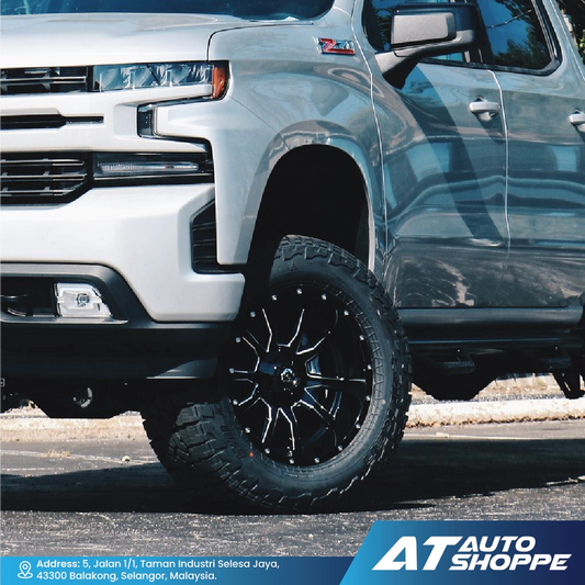 Close-up of a truck with black wheels and tires, parked on a paved surface.
