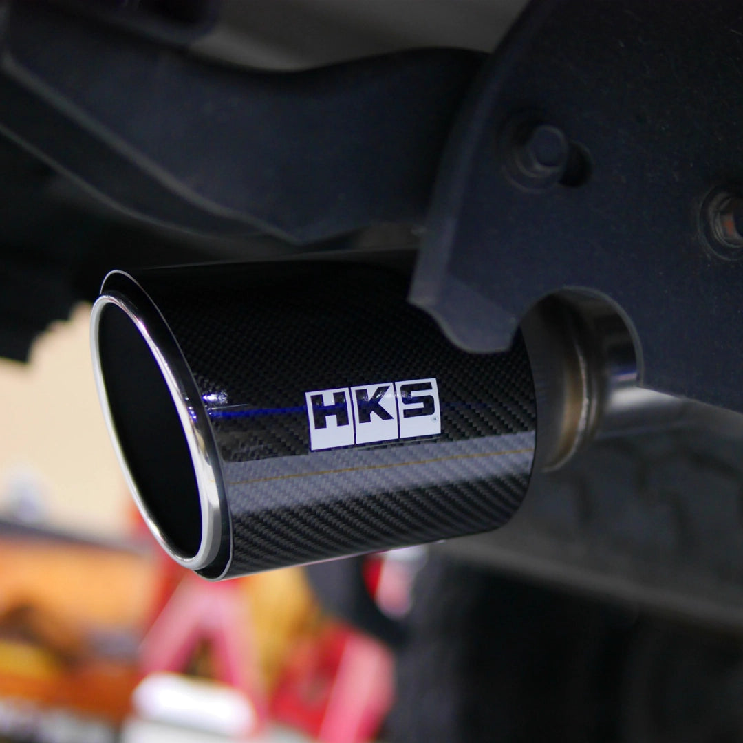 Carbon fiber exhaust tip with HKS logo on a blurred background