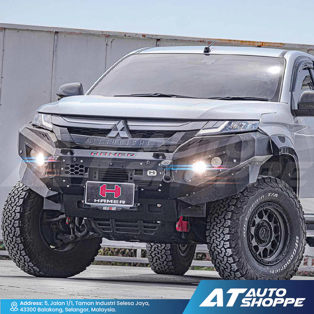 White Mitsubishi truck with large off-road tires on a concrete surface, featuring the AT Auto Shoppe logo.
