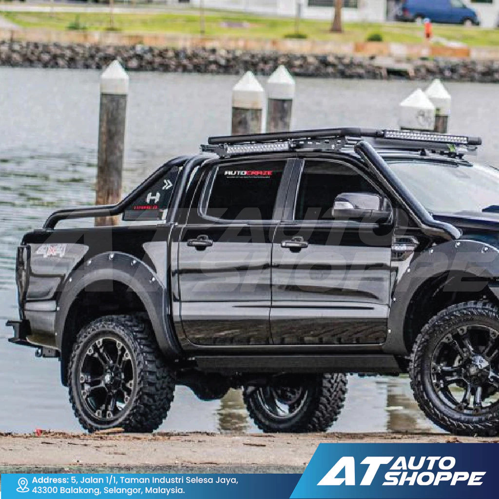 Black pickup truck with roof rack and off-road tires by a waterfront, featuring AT Auto Shoppe branding.