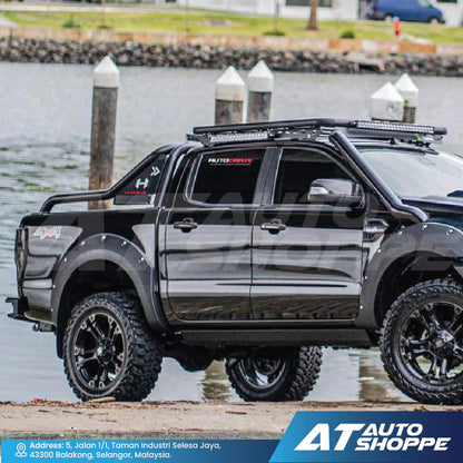 Black pickup truck with roof rack and off-road tires by a waterfront, featuring AT Auto Shoppe branding.