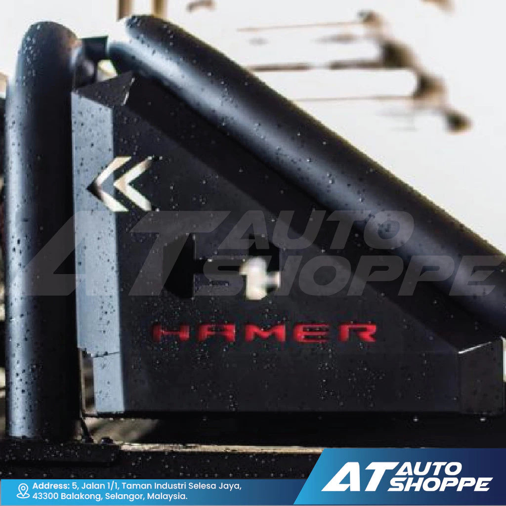 Black metal bracket with 'Hamer' branding on a blurred background with 'AT Auto Shoppe' branding.