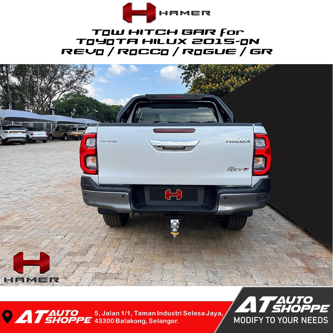 Toyota Hilux with a tow hitch bar on a paved area, featuring Hamer and AT Auto Shoppe branding.