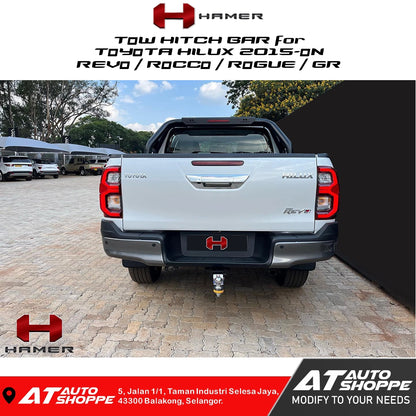 Toyota Hilux with a tow hitch bar on a paved area, featuring Hamer and AT Auto Shoppe branding.