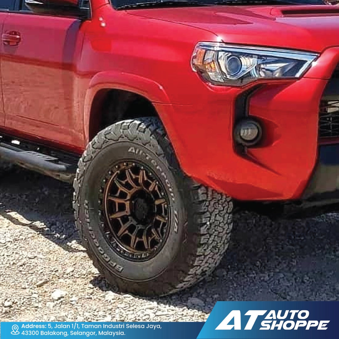 Red Toyota truck with off-road tire and wheel on a gravel surface, featuring AT Auto Shoppe branding.