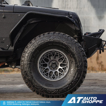 Close-up of a black off-road vehicle tire with tread pattern on a blurred background, featuring AT Auto Shoppe branding.