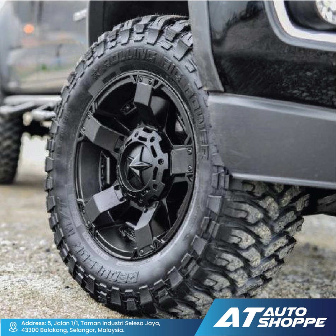 Close-up of a black off-road tire with a detailed rim on a vehicle, featuring the AT Auto Shoppe logo.