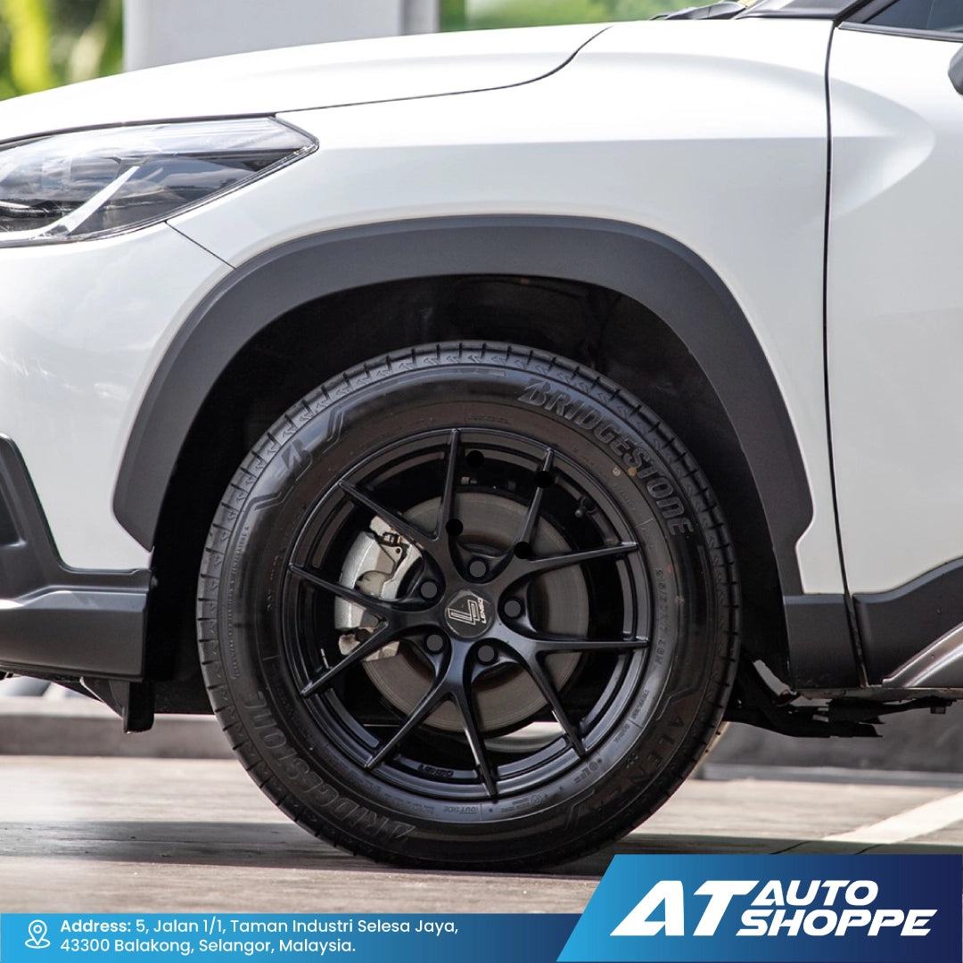 Close-up of a car wheel with black rim and tire on a white car, featuring AT Auto Shoppe branding.