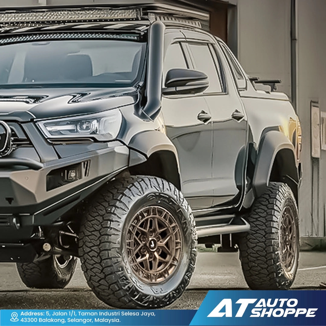 Silver off-road truck with large tires and additional lights in a garage setting, featuring AT Auto Shoppe branding.