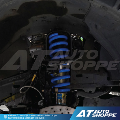 Close-up of a car suspension system with blue shock absorbers, branded 'AT Auto Shoppe'.