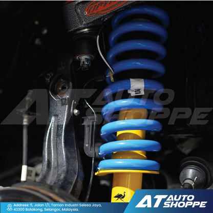 Close-up of a car suspension system with blue and yellow shock absorbers, branded 'AT Auto Shoppe'.