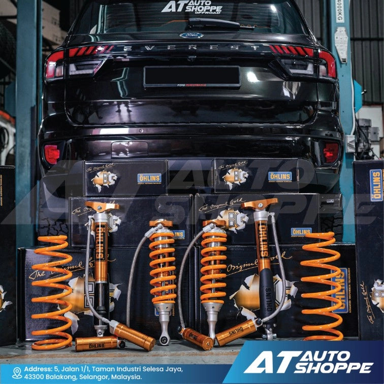 Set of orange Ohlins shock absorbers in packaging displayed on a black vehicle with AT Auto Shoppe branding.