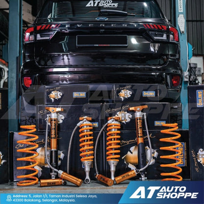 Set of orange Ohlins shock absorbers in packaging displayed on a black vehicle with AT Auto Shoppe branding.