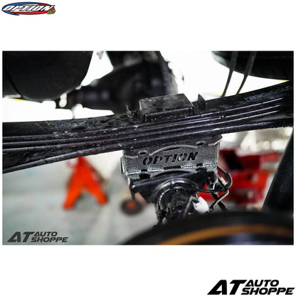 Close-up of a car suspension system with 'Option' branding, blurred background with 'AT Auto Shoppe' branding.