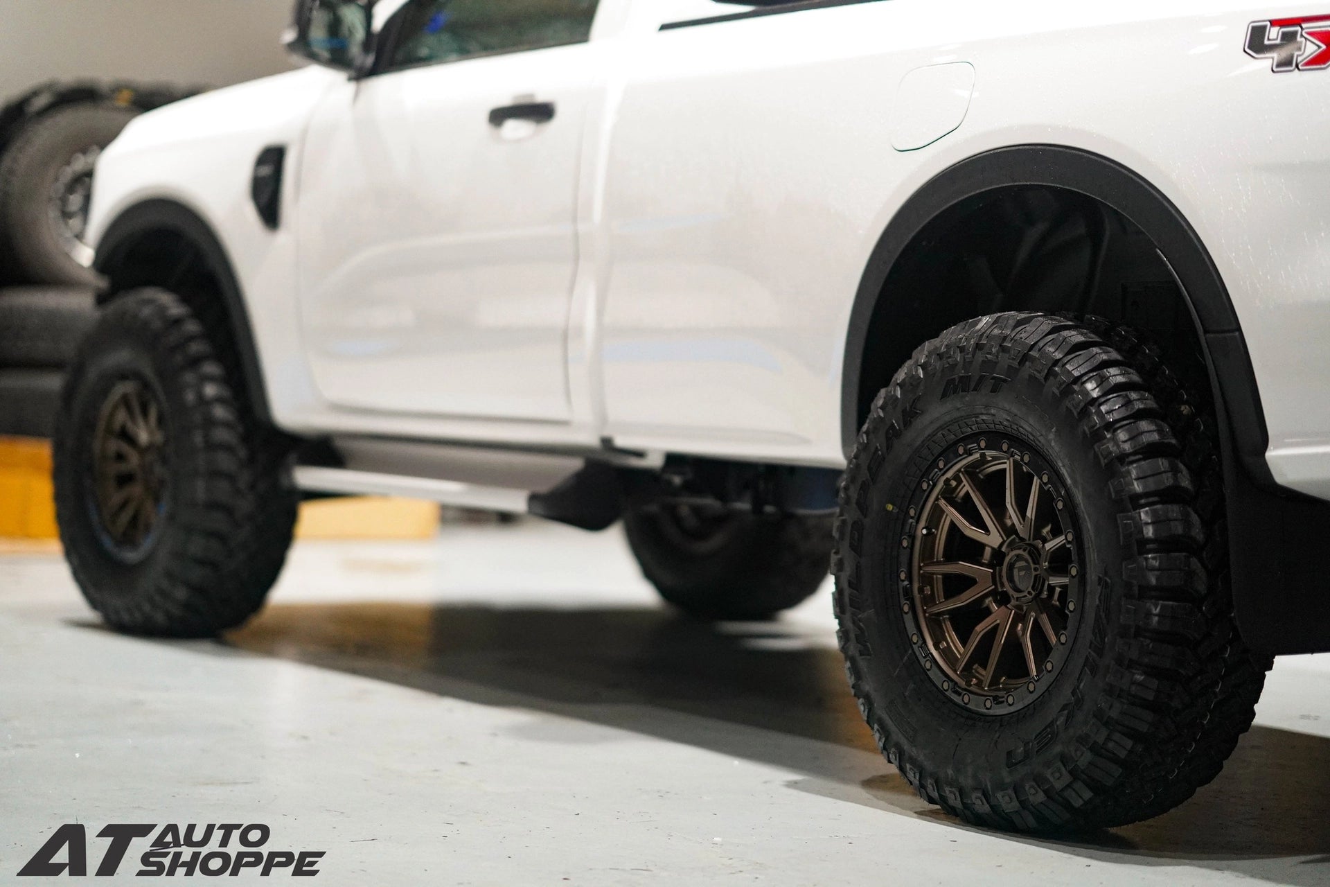 Close-up of a white truck with large off-road tires on a concrete surface.