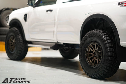 Close-up of a white truck with large off-road tires on a concrete surface.