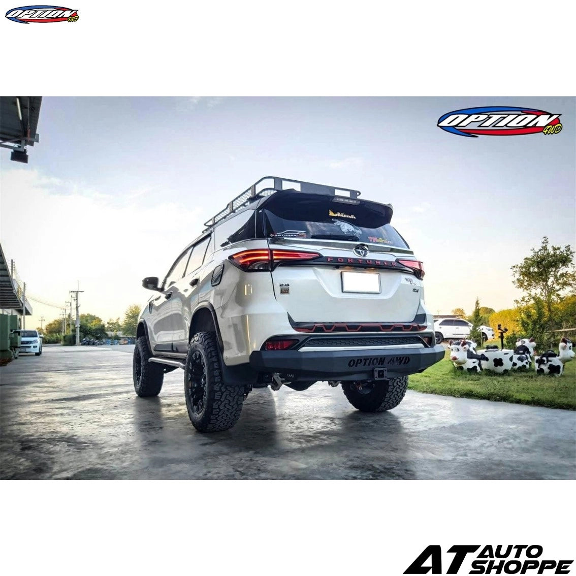 White SUV with additional lights and equipment on a paved surface, with 'AT Auto Shoppe' branding.