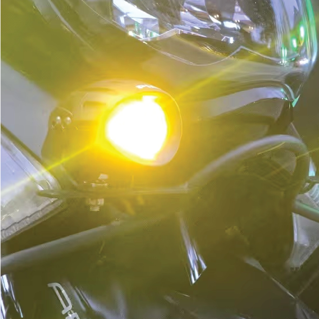 Close-up of a motorcycle headlight with a bright yellow light on a blurred background
