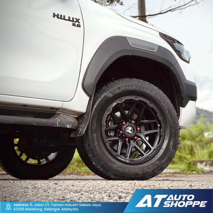 Close-up of a white Toyota Hilux with black wheels on a road, featuring AT Auto Shoppe branding.