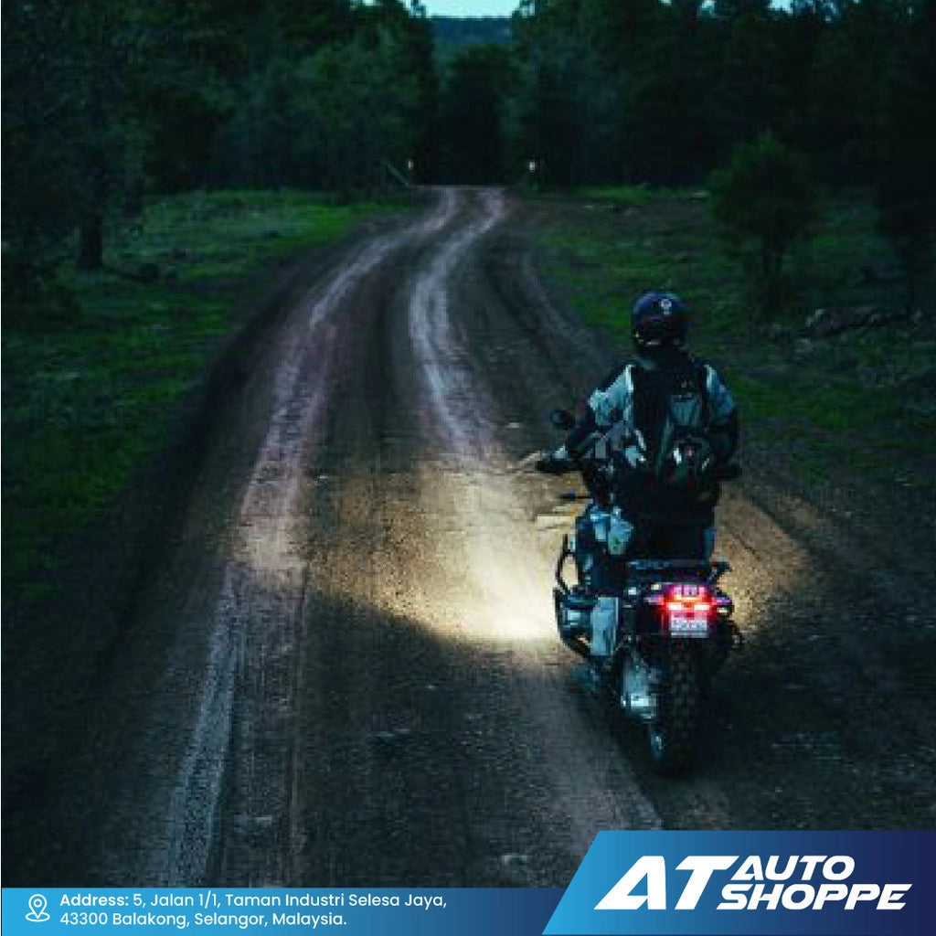 Person riding a motorcycle on a dark forest road with 'AT Auto Shoppe' branding.