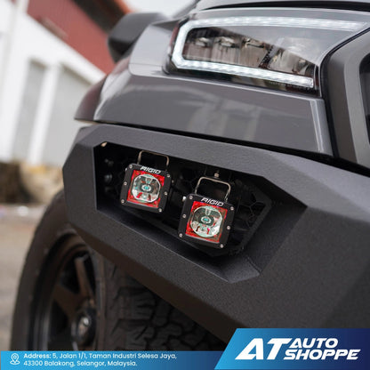 Close-up of a vehicle's front bumper with Rigid lights attached, branded with AT Auto Shoppe.