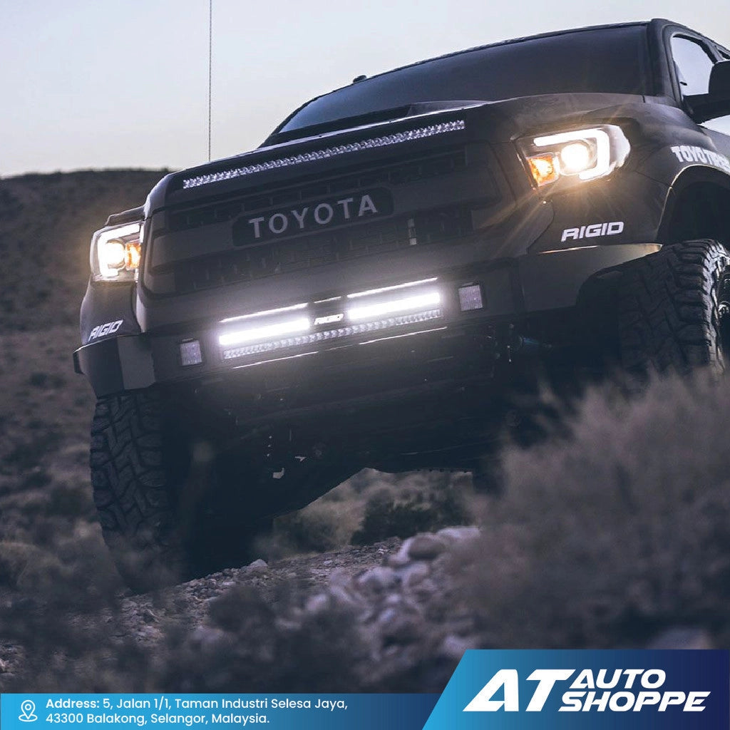 Toyota truck with Rigid lights in a rugged terrain, featuring AT Auto Shoppe branding.