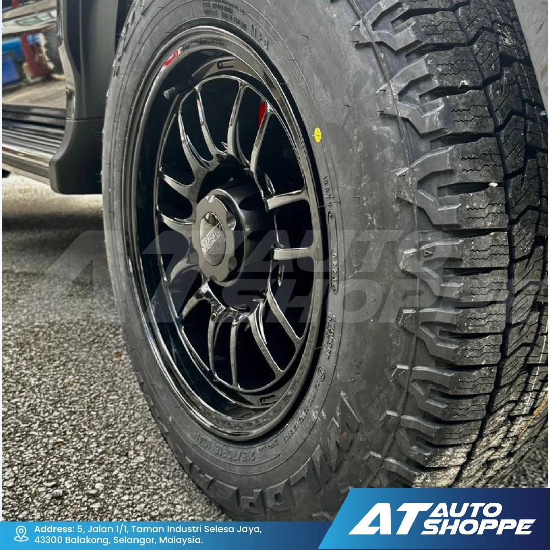 Close-up of a car tire with a black rim on a road, featuring AT Auto Shoppe branding.