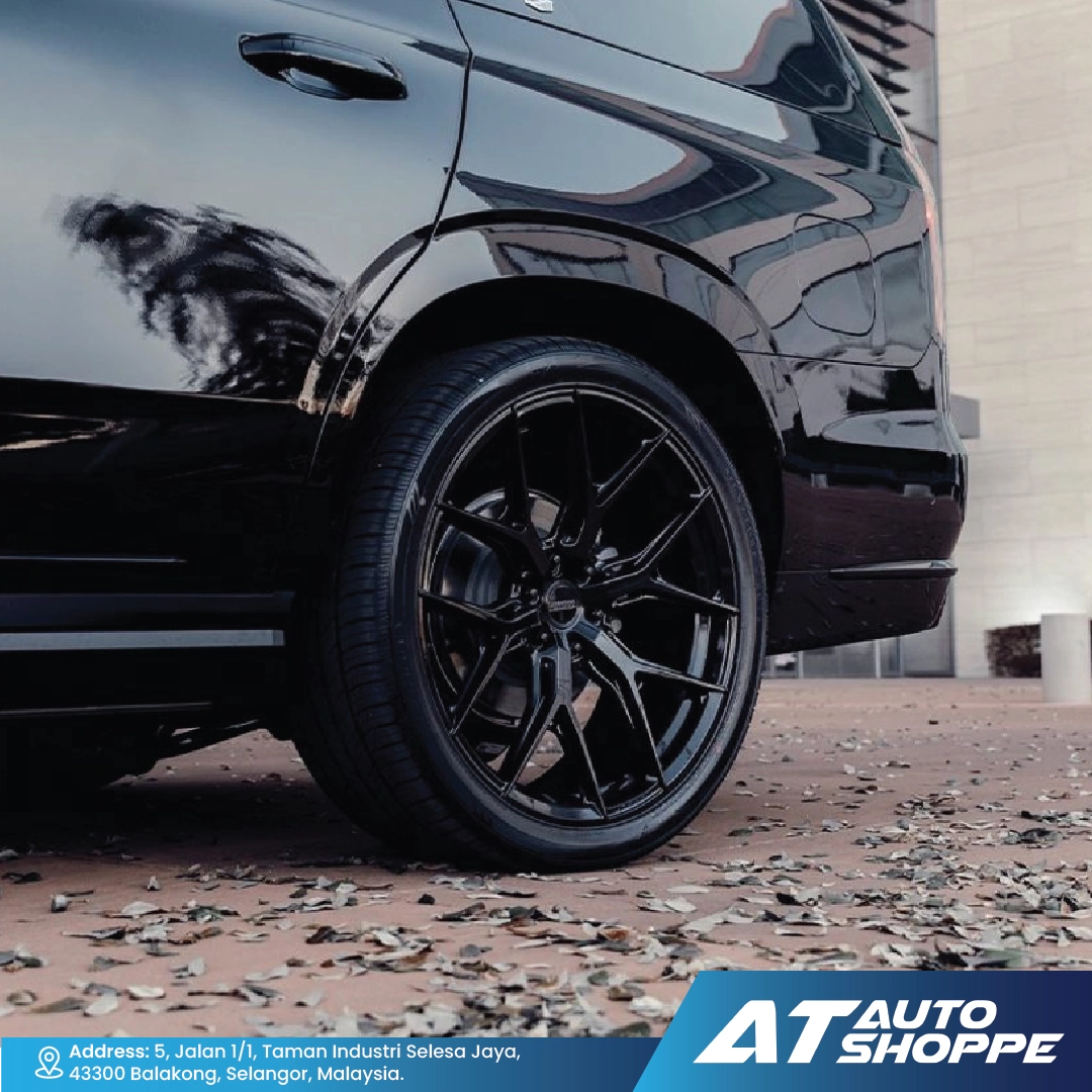 Close-up of a black car wheel with a blurred background, featuring the AT Auto Shoppe logo.