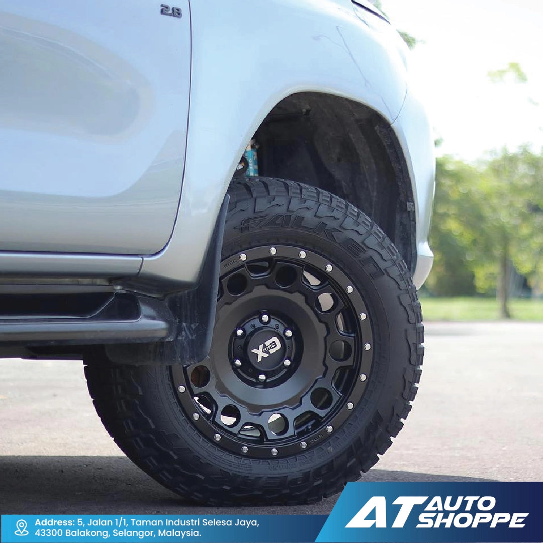 Close-up of a truck tire with a black XD rim on a road, featuring AT Auto Shoppe branding.
