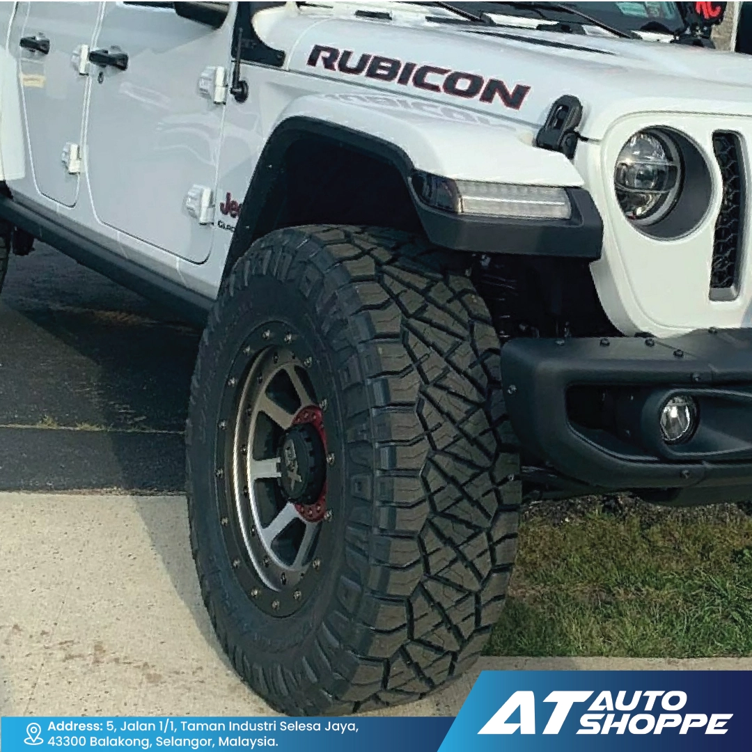 White Jeep Rubicon vehicle with large off-road tire on a paved surface, featuring 'AT Auto Shoppe' branding.