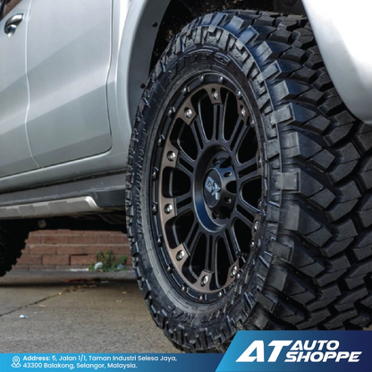 Close-up of a truck tire with a rugged tread pattern, mounted on a black XD rim, with 'AT Auto Shoppe' branding.