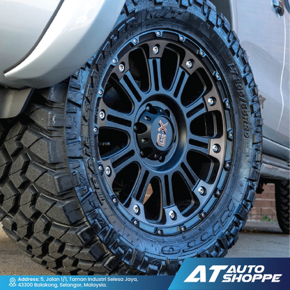 Close-up of a black off-road tire with visible tread pattern on a vehicle, featuring the AT Auto Shoppe logo.