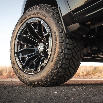 Close-up of a tire with a detailed tread pattern on a vehicle, set against a blurred natural background.