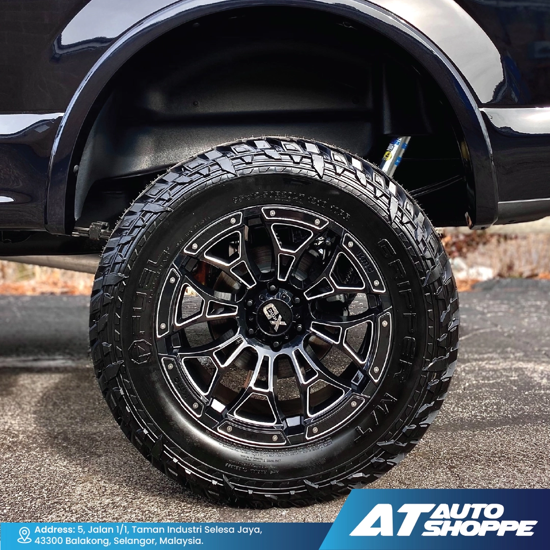 Close-up of a black off-road tire and rim on a vehicle, with AT Auto Shoppe branding.