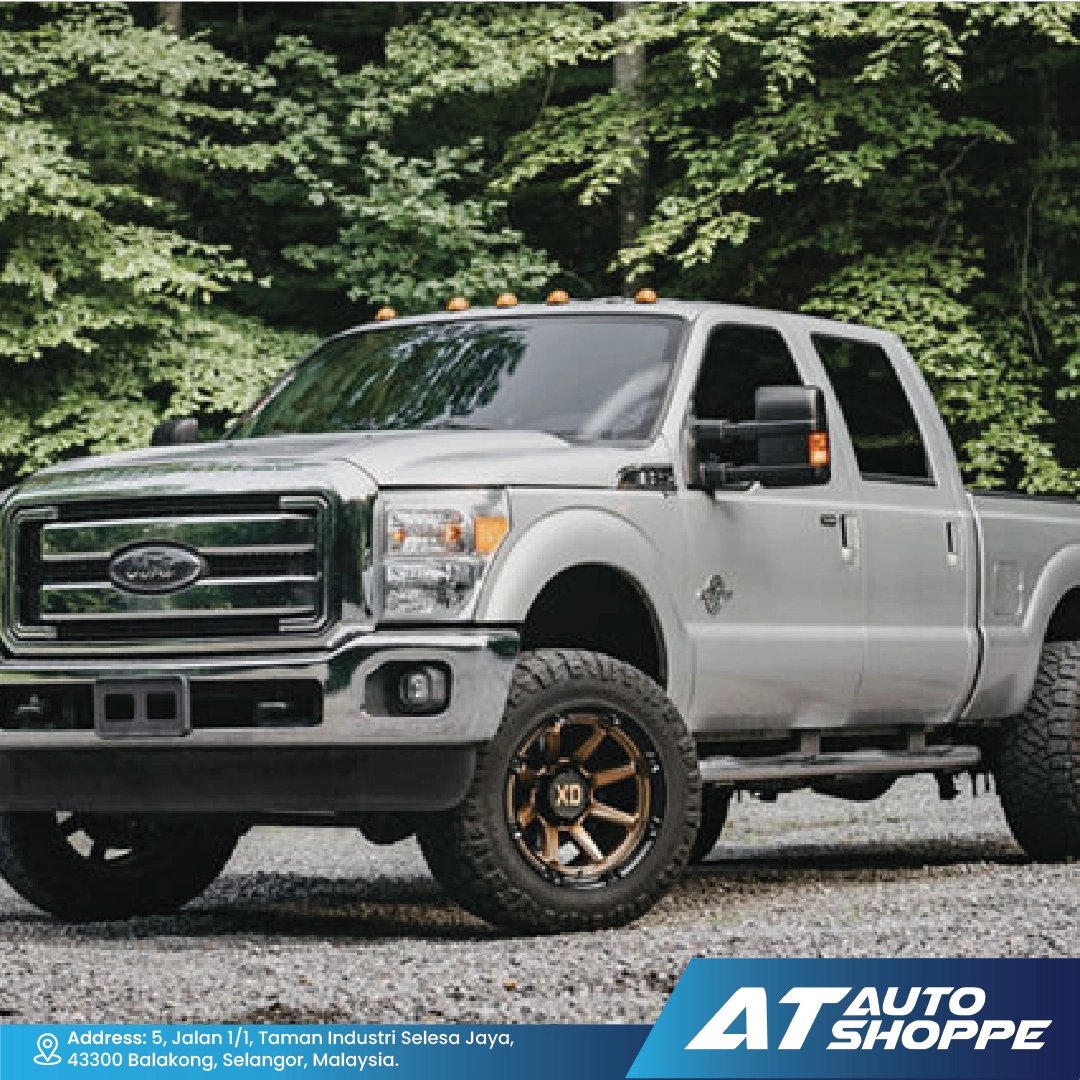 Silver Ford truck parked on a gravel road with trees in the background, featuring AT Auto Shoppe branding.